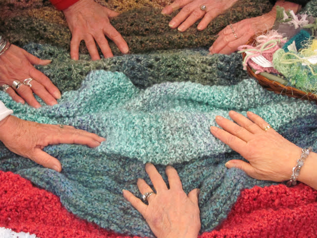 Hands resting on prayer shawls made by the Prayer Shawl Circle.
